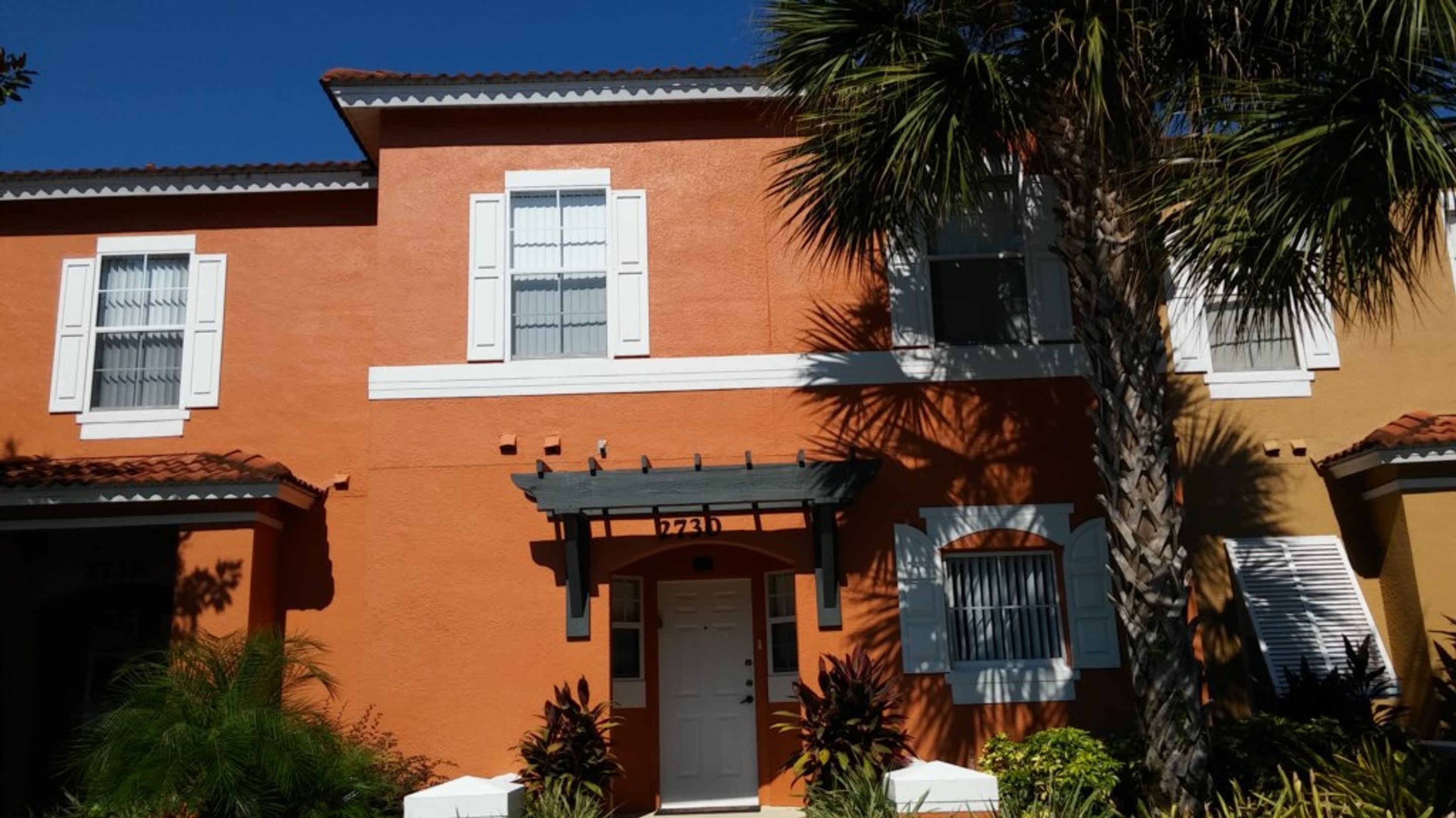 A two-story building with a red facade, white shutters, and a central entrance with a door marked "2730".