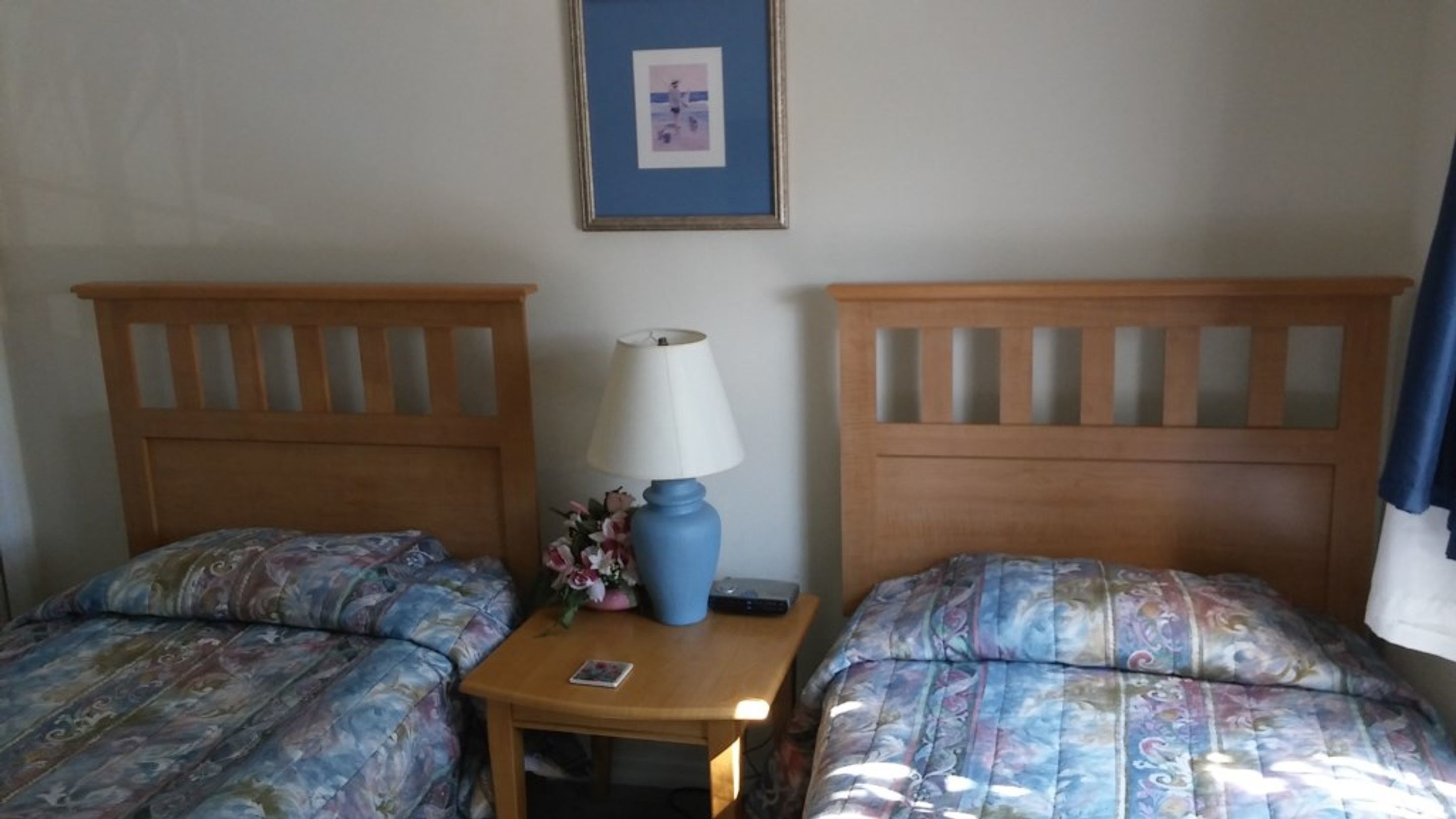 A hotel room with two beds, a nightstand with a lamp, and a framed picture on the wall.
