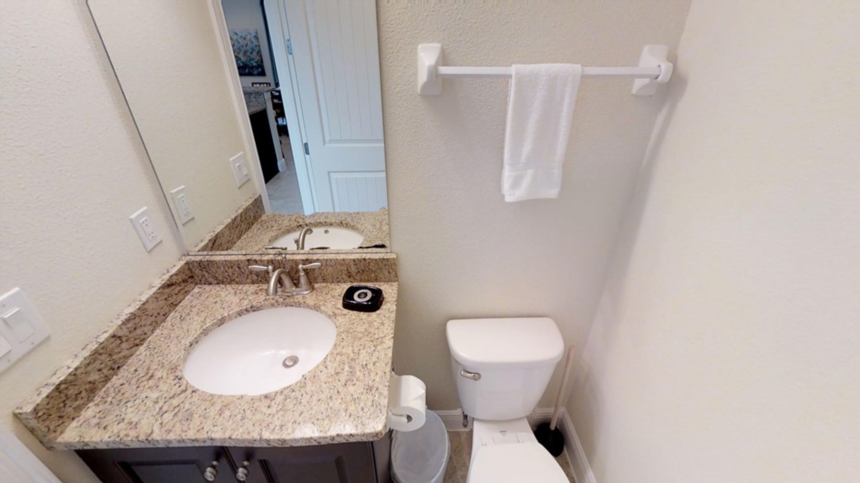 A bathroom with a granite countertop sink, a toilet, and a towel rack.