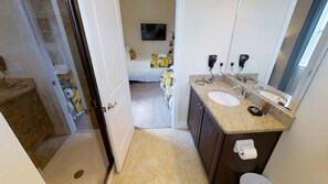 Ein Badezimmer mit Waschbecken, Spiegel und Toilette. Ein Duschbereich ist durch eine Glastür erkennbar.