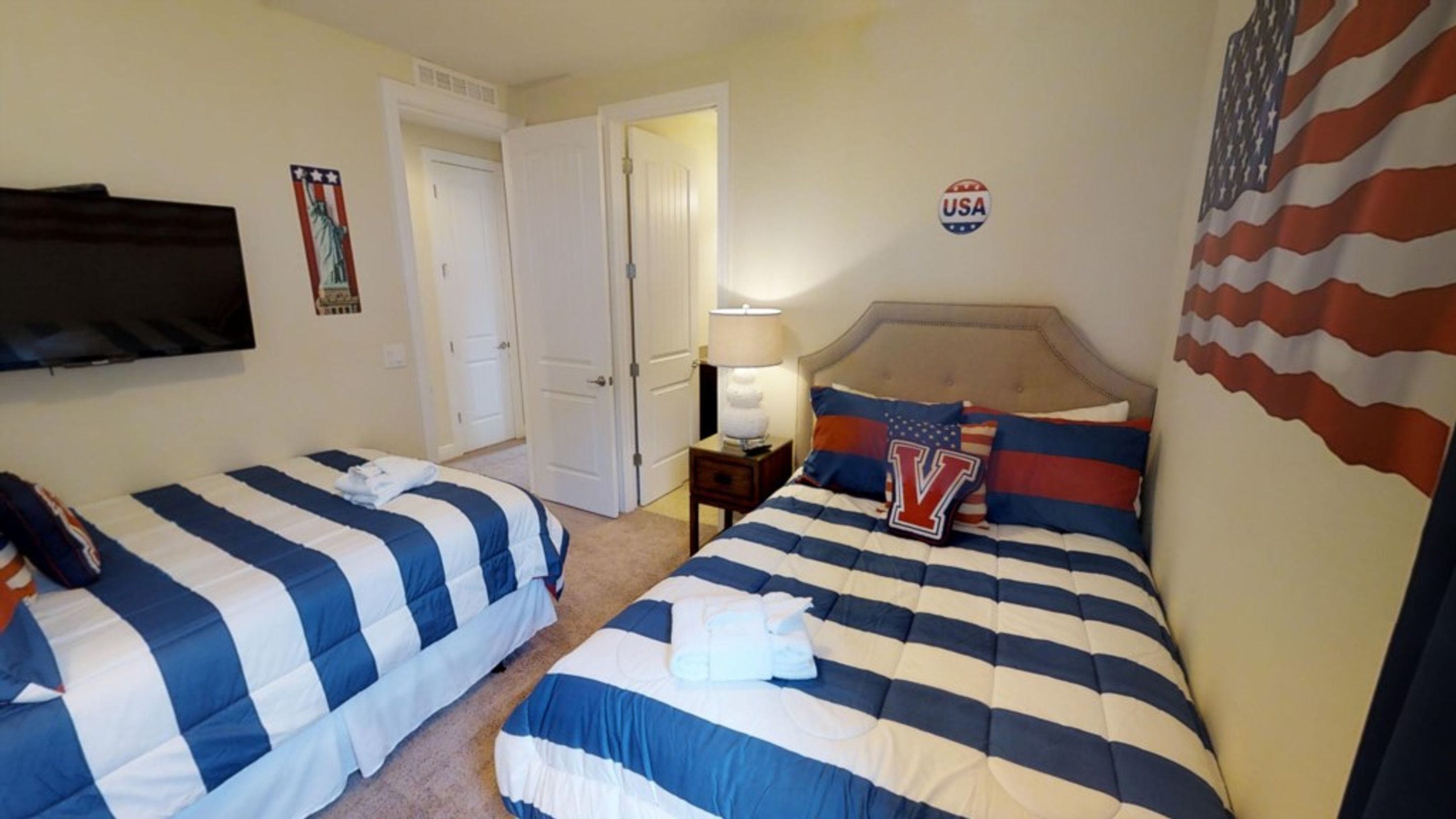 A hotel room with two beds, a TV, a USA flag, and a door leading to another room.
