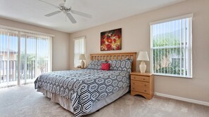 A bedroom with a bed, two bedside tables, a ceiling fan, and large windows with blinds. - Regal Oaks 2713 (Kissimmee)