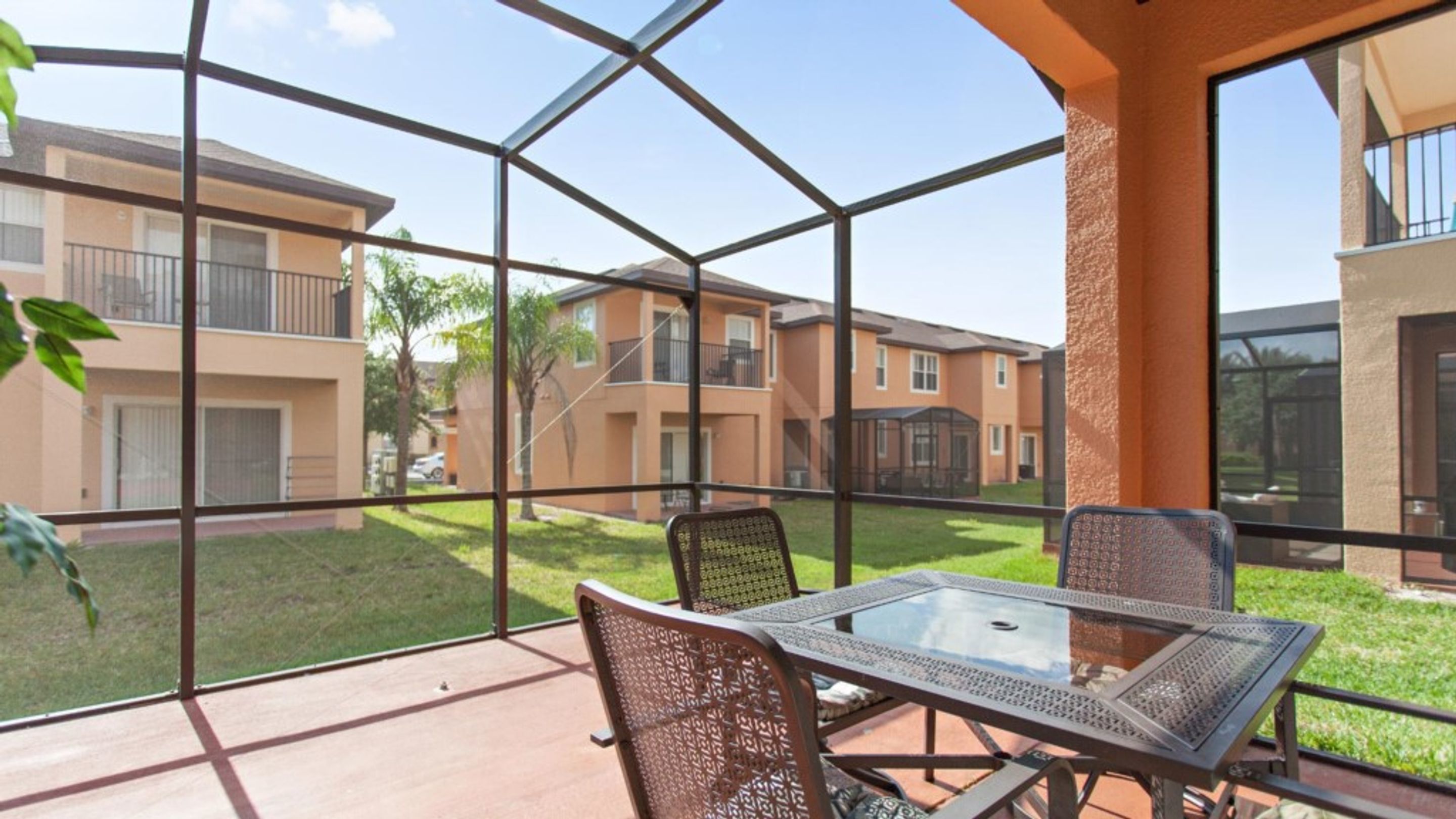 A glass-enclosed patio with a table and chairs, overlooking a residential area with apartment buildings.
