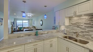 A modern kitchen with white cabinets, a stone backsplash, and pendant lighting.