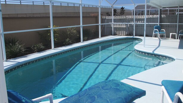 A swimming pool with a covered patio area, lounge chairs, and a view of a bridge in the background. - Indian Wells 5356 (Kissimmee)