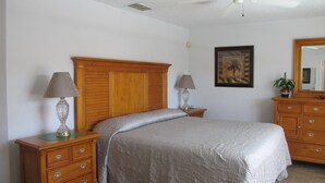 A bedroom with a wooden headboard, two bedside tables with lamps, a bed with a beige comforter, a wooden dresser, and a framed picture on the wall. - Indian Wells 5356 (Kissimmee)