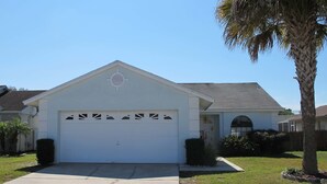 A single-story house with a white garage, a small front yard, and a palm tree. - Indian Wells 5356 (Kissimmee)