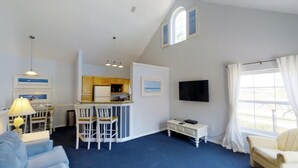 A compact living space with a kitchenette, a dining area with bar stools, a flat-screen TV, and a large window with curtains.
