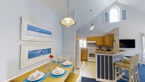 A dining area with a wooden table set for four, a kitchen with wooden cabinets, and a TV mounted on the wall.
