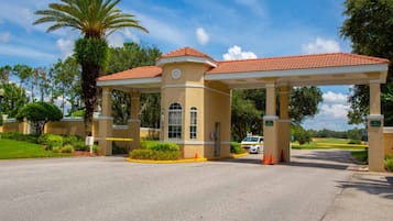 A building with a red-tiled roof and beige walls, surrounded by greenery and palm trees.