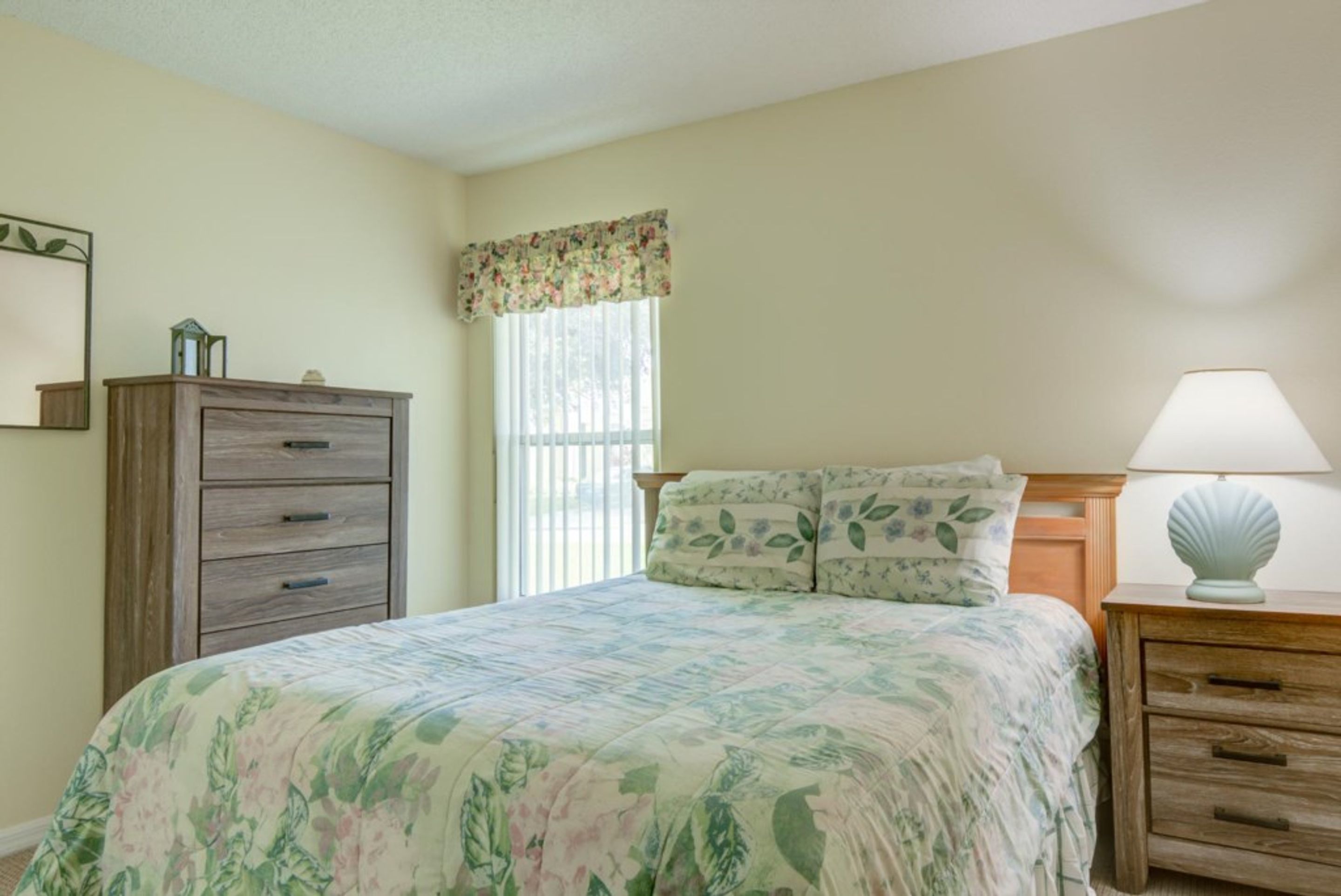 A bedroom with a bed, a dresser, a nightstand, and a window with a floral valance.