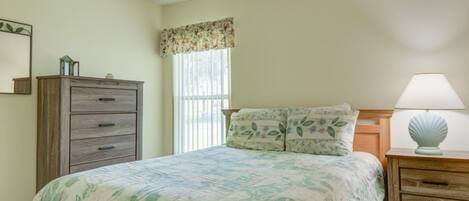 A bedroom with a bed, a dresser, a nightstand, and a window with a floral valance.