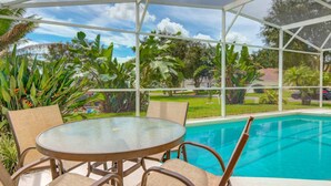 A covered outdoor area with a pool, a round table, and chairs.