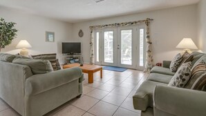 A living room with two sofas, a coffee table, a TV, and a large window with curtains.