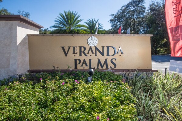 A sign for Veranda Palms with a logo, surrounded by greenery and palm trees.
