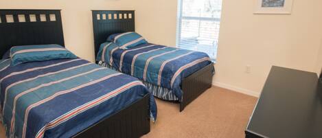 A bedroom with two beds, a window, and a desk.