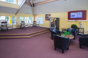 A spacious living area with a high ceiling, a television mounted on the wall, and a vending machine.
