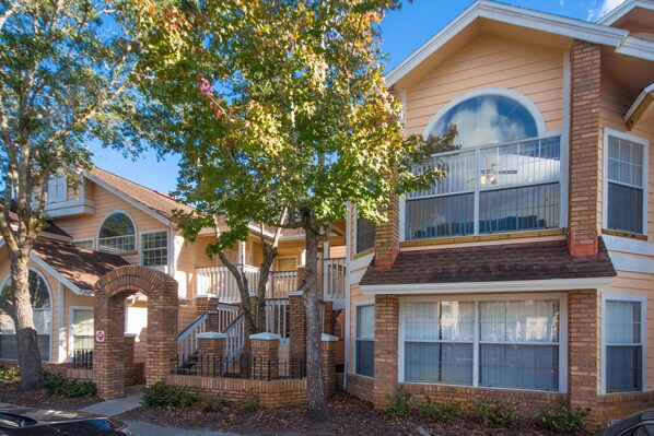 A multi-story residential building with a brick facade, large windows, and a covered front porch.