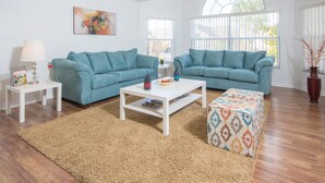 Un salon avec deux canapés de couleur turquoise, une table basse blanche et un pouf à motifs.