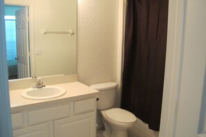 A bathroom with a white sink, toilet, and dark shower curtain. - Windsor Hills 7735 (Kissimmee)