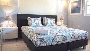 A neatly made bed with patterned bedding and pillows, two bedside lamps, and a framed picture on the wall. - Noord 2 (Noord)