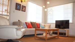 A living room with a sofa, a coffee table, a television, and a chair. - Noord 2 (Noord)
