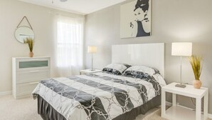 Een slaapkamer met een bed, nachtkastjes, een plafondventilator, een raam met gordijnen en een spiegel aan de muur.