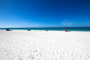 A wide sandy beach with footprints, a tent, and a red umbrella.