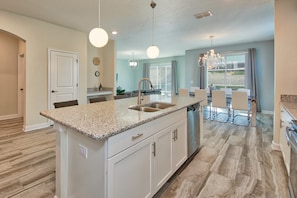 A modern kitchen with a central island, white cabinetry, and a stainless steel sink. - Champions Gate 1560 (Davenport)