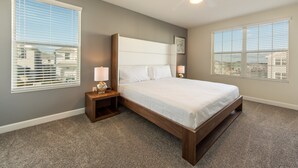 Ein Schlafzimmer mit Bett, Nachttischen, Deckenventilator und großen Fenstern mit Jalousien.