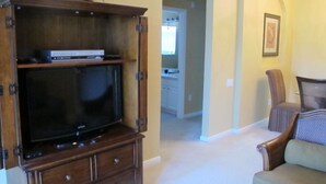 Ein Wohnzimmer mit einer Holz-Unterhaltungsanlage, einem Fernseher, einer Couch und einem Essbereich im Hintergrund.