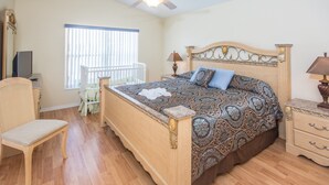 A bedroom with a wooden bed, a chair, a nightstand, a lamp, and a window with blinds.