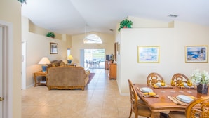 A spacious living room with a sofa, a dining table set for four, and a view of the patio through a large window.
