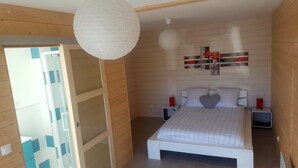 A bedroom with a bed, two bedside tables, a wall-mounted artwork, and a hanging light fixture.