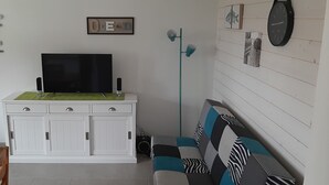 A living room with a flat-screen TV, white cabinets, a green mat, a patterned sofa, and a clock on the wall.