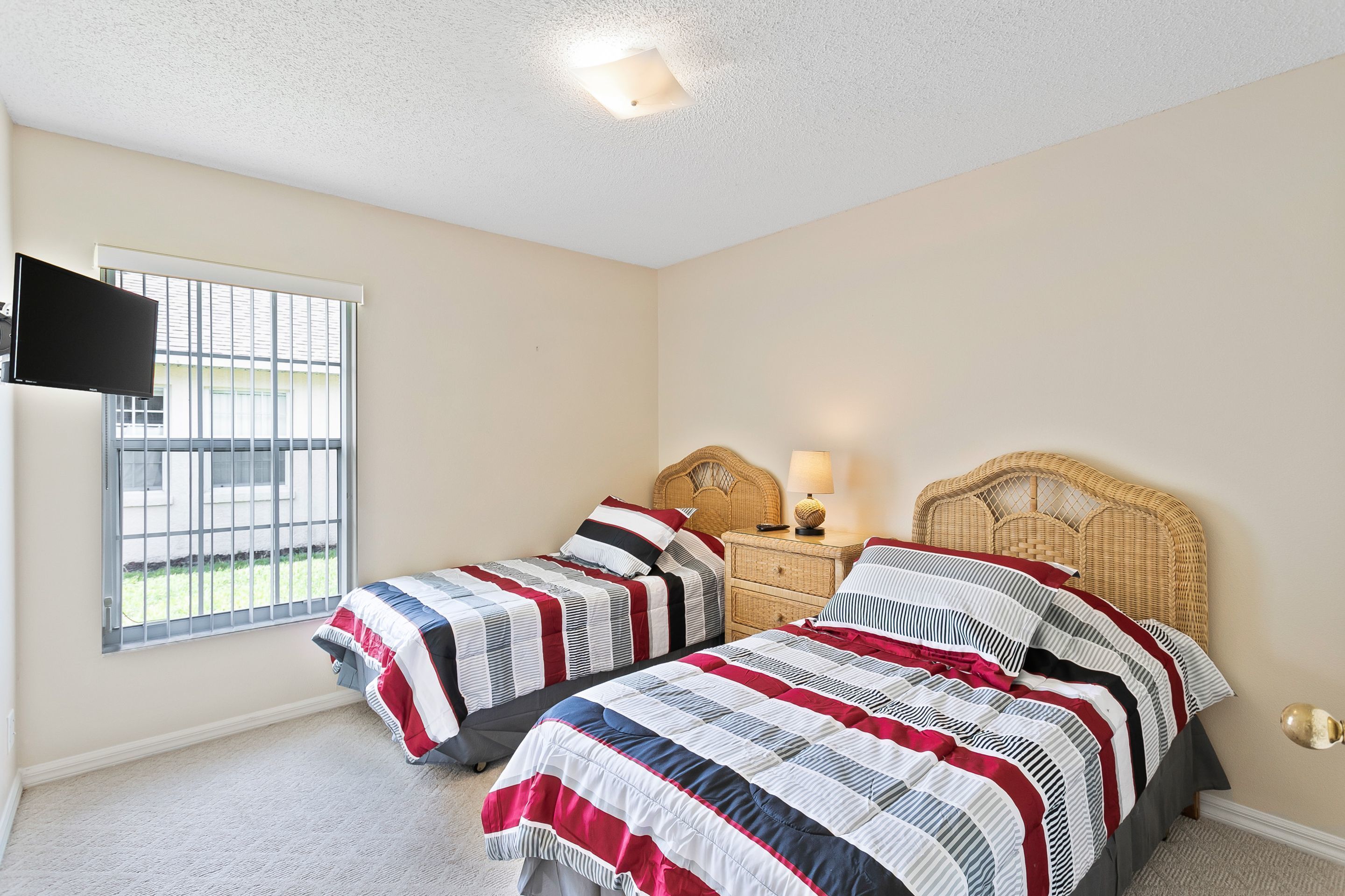 A bedroom with two beds, a television, a window with bars, and a nightstand with a lamp.