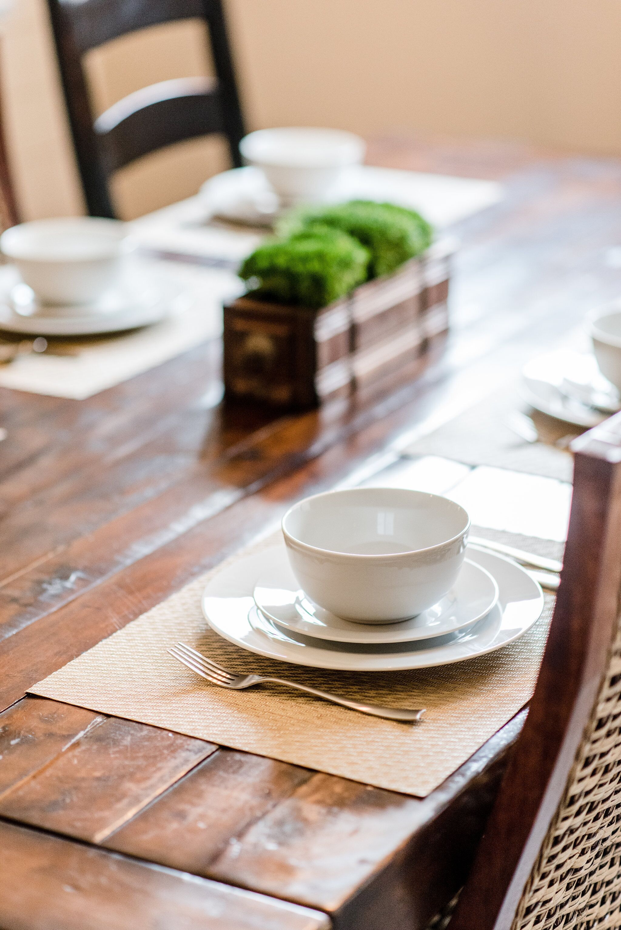 A wooden dining table with white plates, bowls, and cutlery.