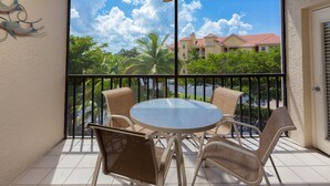 A balcony with a round table and four chairs, offering a view of a building with a red roof and palm trees. - Fort Myers Beach Area 7327 - 311 (Fort Myers Beach)