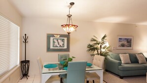 A dining area with a glass table, chairs, a hanging light fixture, a green sofa, and framed artwork on the walls. - Fort Myers Beach Area 7327 - 311 (Fort Myers Beach)