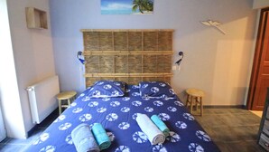 Een slaapkamer met een bed, twee krukken, een radiator, een schilderij van een strand en een houten hoofdeinde.