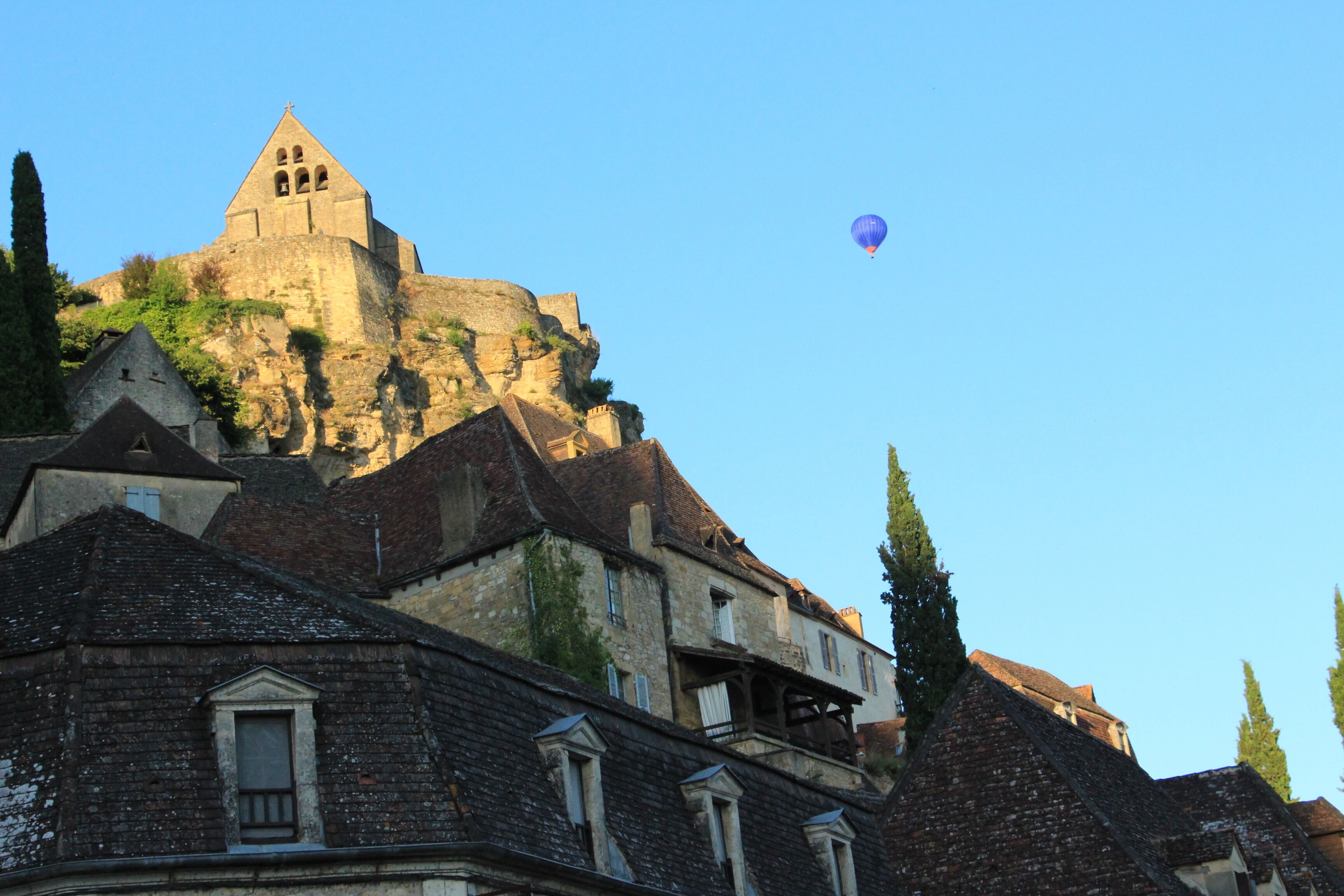 A historic building with a prominent tower, surrounded by traditional architecture and a clear sky.