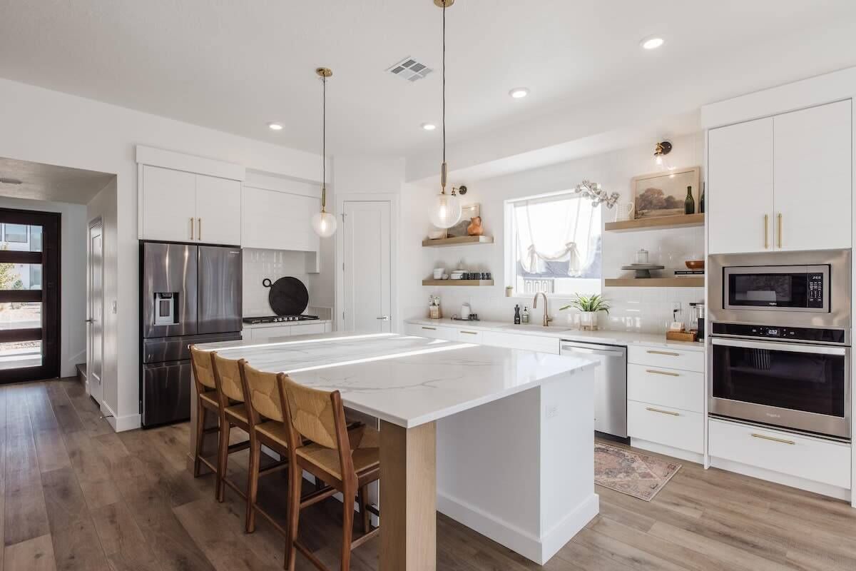 A modern kitchen with white cabinetry, stainless steel appliances, and a central island with bar stools.