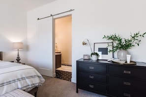 A bedroom with a bed, bedside table, dresser, and a door leading to a bathroom.