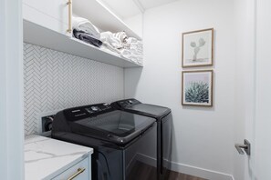 A laundry area with a black washer and dryer, a white tiled wall, and two framed pictures.