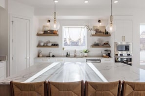 A modern kitchen with a marble countertop, pendant lights, and built-in appliances.