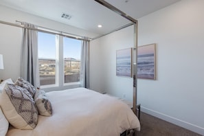 A bedroom with a large bed, a window with curtains, and two framed pictures on the wall.