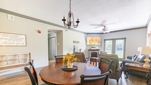 A dining area with a round table, chairs, and a chandelier. There is a sofa and a television in the background. - Updated Clean Spacious 3BR/2BA Condo right off the parkway! Pools/WiFi/Grills (Pigeon Forge)