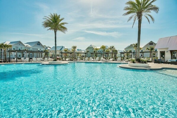 A large swimming pool with multiple lanes, surrounded by palm trees and houses.