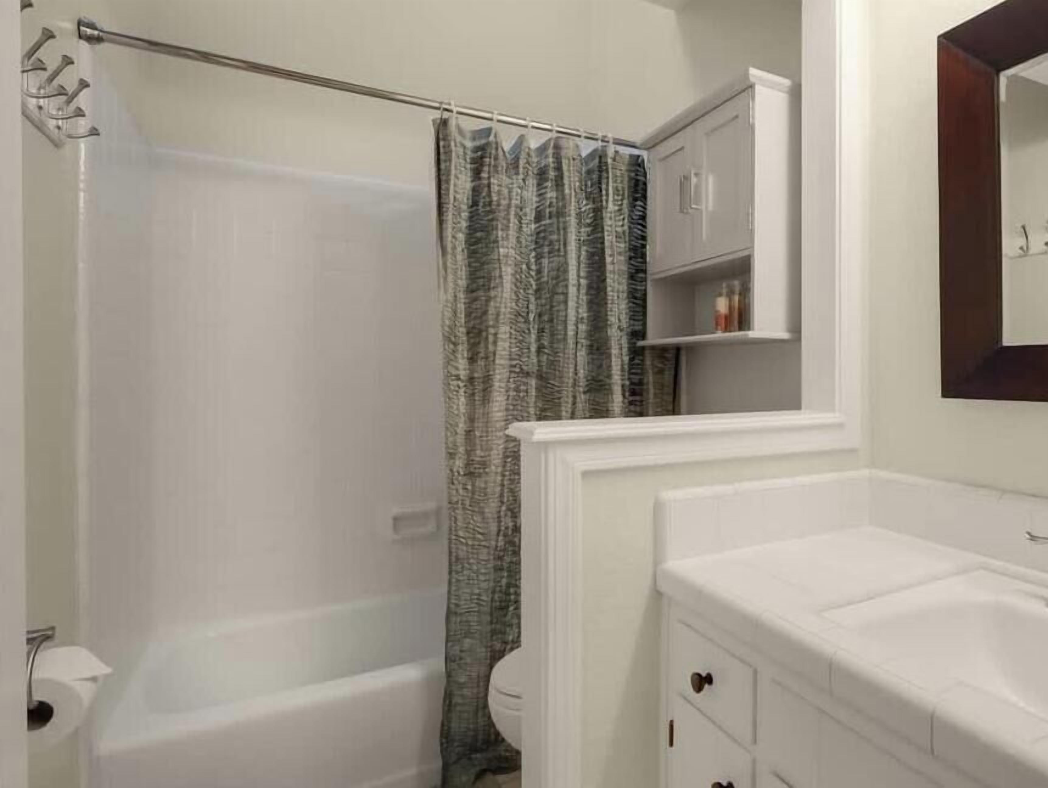 Ein Badezimmer mit Badewanne, Duschvorhang, Toilette und Waschtisch mit Schubladen.