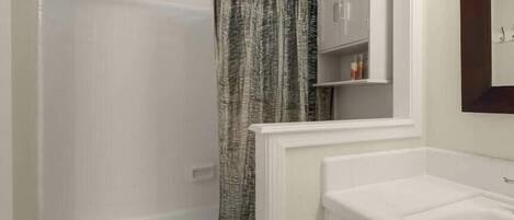 Ein Badezimmer mit Badewanne, Duschvorhang, Toilette und Waschtisch mit Schubladen.